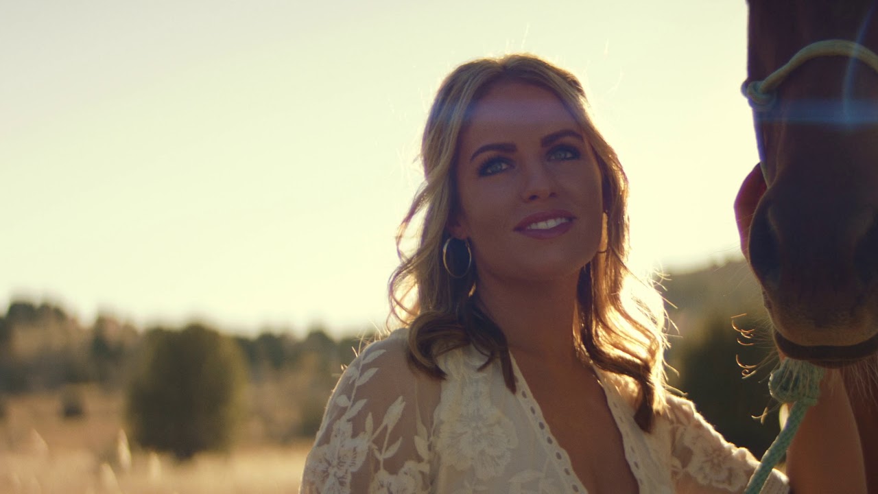 A woman standing beside a horse in the She Loves Horses music video